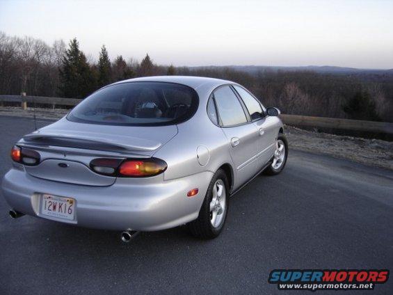 Silver 1999 Ford Taurus sedan with a rear spoiler, parked on a road with trees in the background