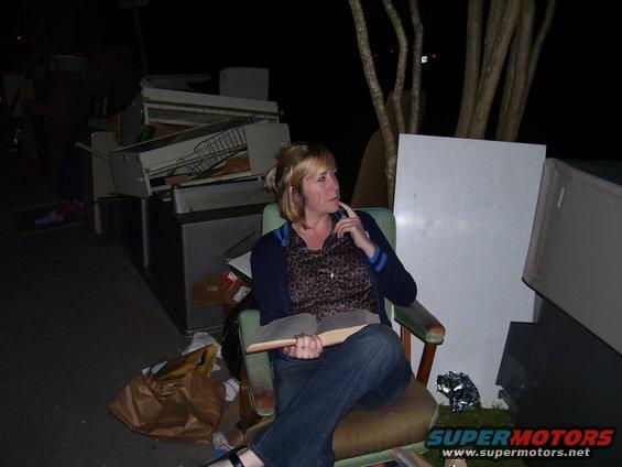 Woman in chair with discarded furniture and debris, dark outdoor setting