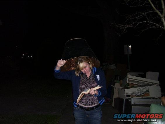 Woman wearing a large lampshade on her head, reading a book outdoors at night