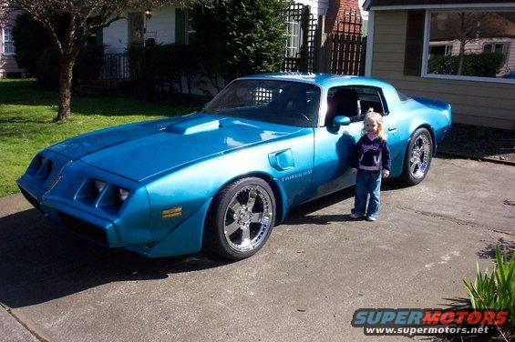 Blue 1979 Pontiac Trans Am parked in a driveway with a young girl standing next to it