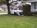 2005 Toyota Camry - A white 2005 Toyota Camry has crashed into a tree and a bush, sustaining significant front-end damage.