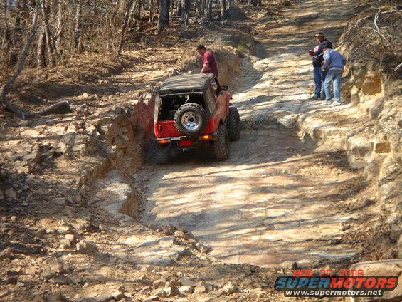 red SUV navigating rocky trail, people watching