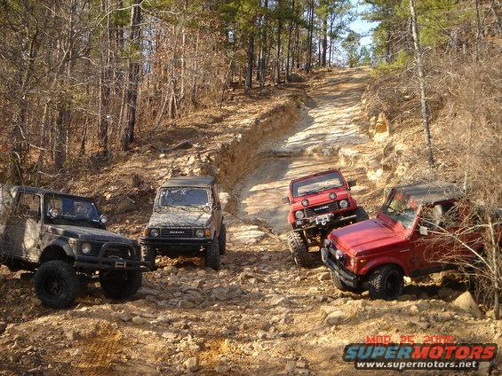 Four Suzuki Samurai SUVs on a rocky, wooded trail