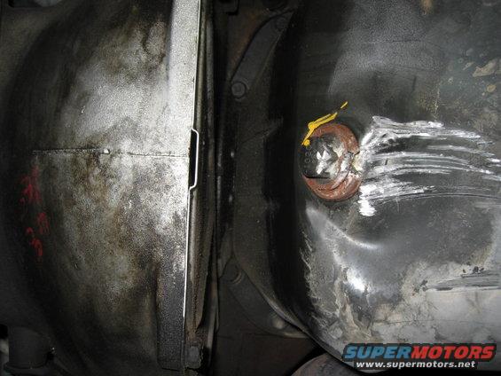 Underside view of a vehicle's fuel tank with a dented cap and a differential housing