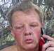1989 Ford Bronco - A man with a red face and blond hair speaks on a cell phone amidst a backdrop of trees.