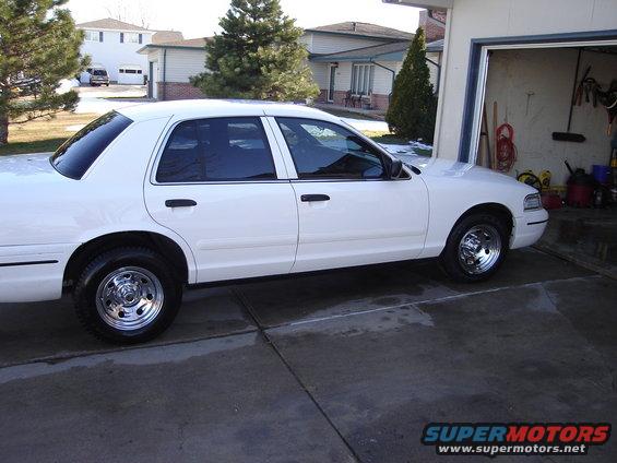 White sedan parked in driveway next to garage. Chrome wheels visible