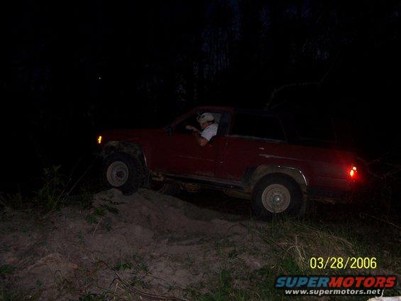 Red SUV driving up a dirt hill at night. Driver is visible