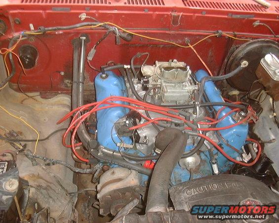 Engine bay with blue valve covers and red spark plug wires. "CAUTION" text visible on fan shroud