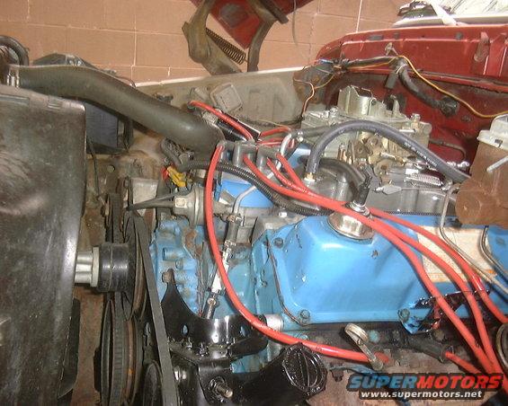 engine bay with blue valve covers, red spark plug wires, and carburetor