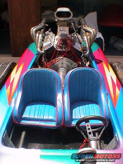 Drag boat interior with two blue seats, exposed V8 engine, and colorful graphics on the sides