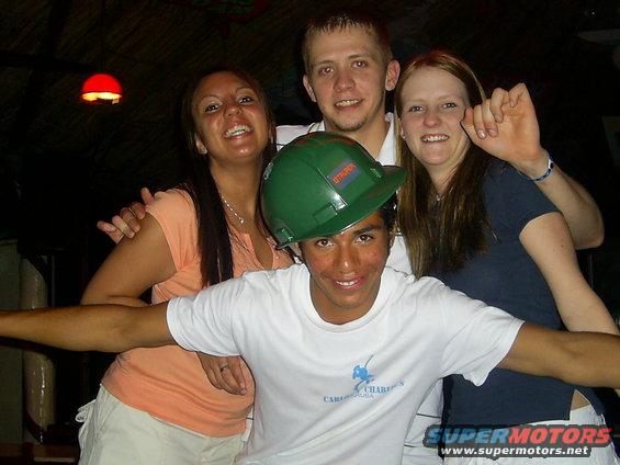 Four people posing for a photo, one wearing a green hard hat
