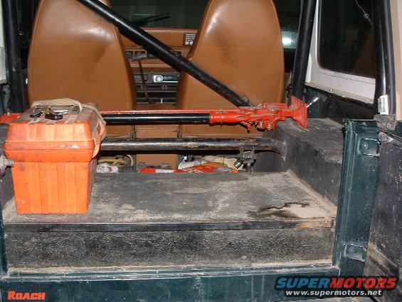 Green Jeep YJ interior, rear cargo area with orange toolbox and red Hi-Lift jack. Brown seats visible