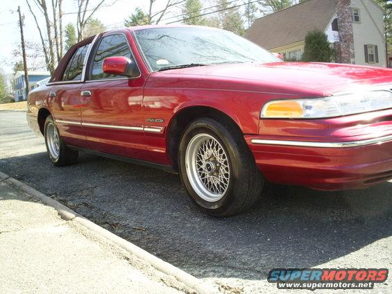 Red sedan parked on a street, showing the front passenger side. It has wire-spoke wheels