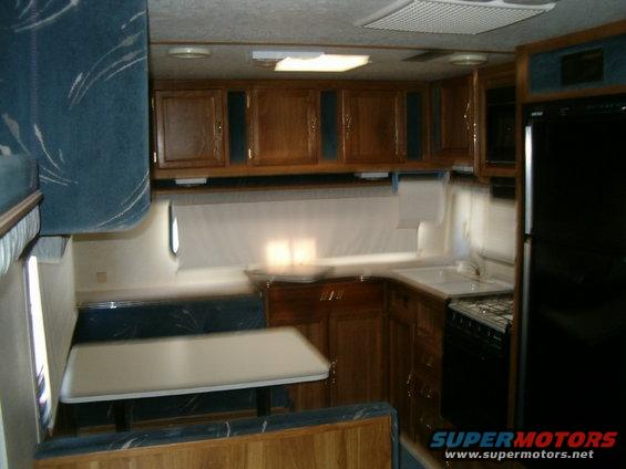 Interior of a trailer with a dinette, kitchen counter, sink, and refrigerator