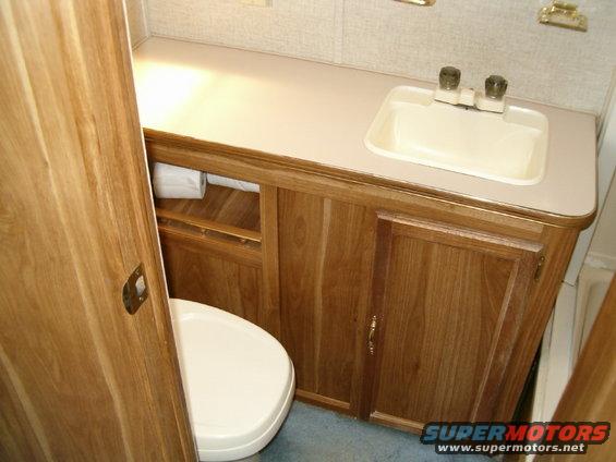 RV bathroom with toilet, sink, and wood cabinets