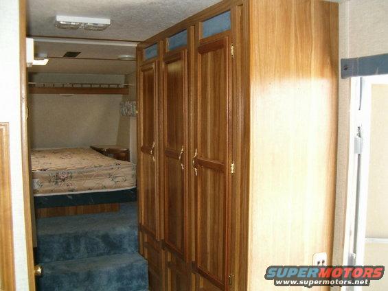 Interior of an RV showing a bed, carpeted steps, and wooden cabinets