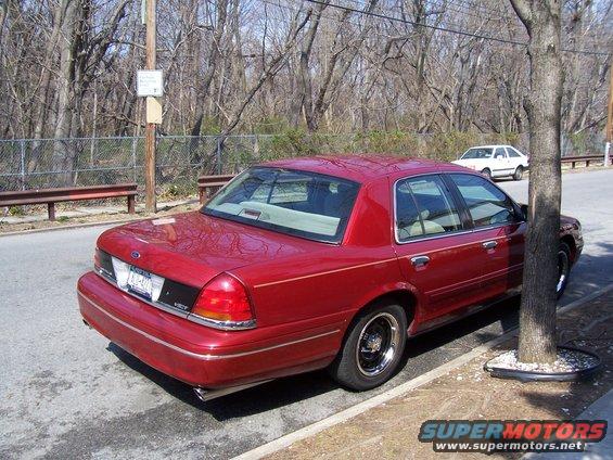Red sedan parked on street, rear 3/4 view. License plate visible