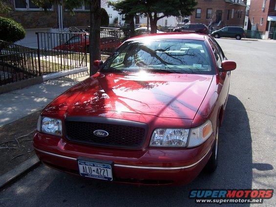 Red Ford Crown Victoria, front view, parked on street. Chrome trim, black grille, New York license plate ALU-4221