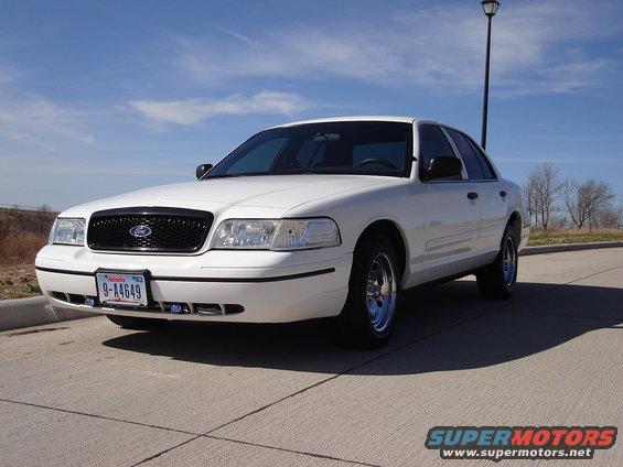 White sedan parked on pavement, blue sky overhead. License plate reads 9-A4649