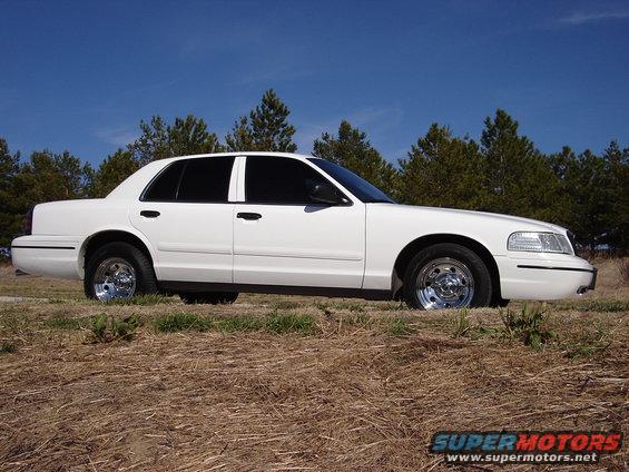 White 2000 Ford Crown Victoria sedan parked on dry grass, side view, chrome wheels, tinted windows