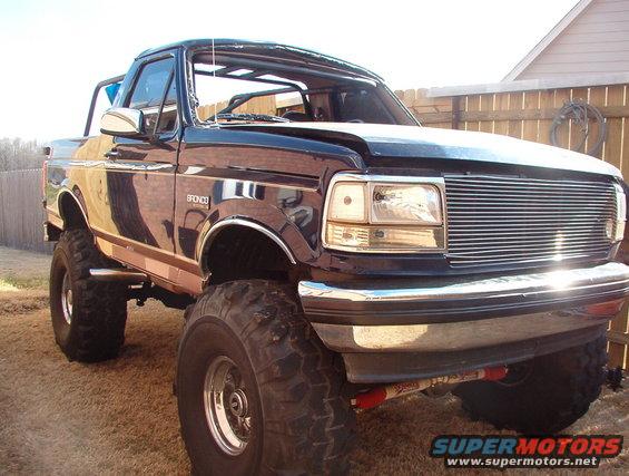 Lifted dark blue Ford Bronco with chrome grille and large tires. Bronco badge visible on the fender