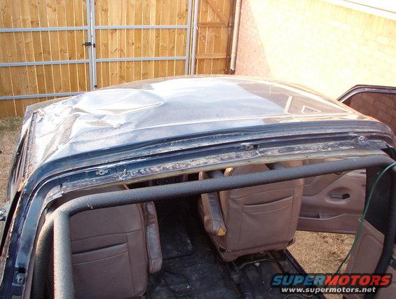 Damaged roof of a dark-colored SUV, showing interior seats and a roll cage