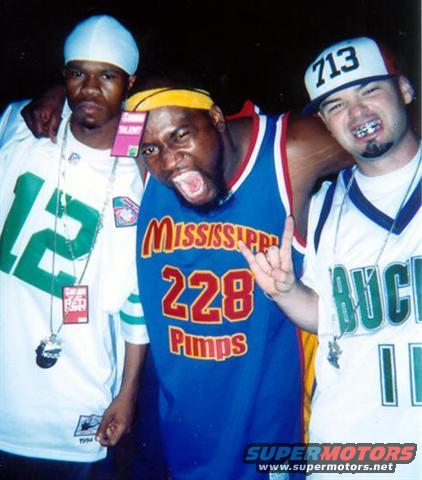 Three men in jerseys and hats pose for a photo; one wears a white jersey with green 12, another a blue jersey with red 'Mississippi 228 Pimps', and the third a white jersey with green 'Bucks 11'