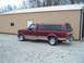 1996 Ford F-150 - A maroon and tan Ford F-150 pickup truck with a camper shell is parked on a gravel lot next to a tan building.