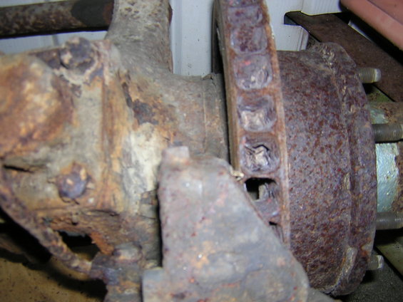 Heavily rusted brake rotor with visible bolt holes and surrounding suspension parts