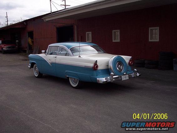 Two-tone blue and white sedan with a continental kit parked in front of a red building