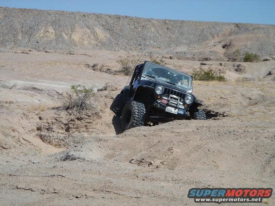 Black Jeep Wrangler going off-road in a sandy, dry wash