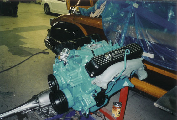 Mopar engine and transmission assembly on a stand, with a woody car in the background