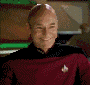 Man in red Starfleet uniform smiling, bald head, close-up