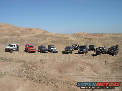 Group of SUVs and trucks parked in a desert with hills in the background