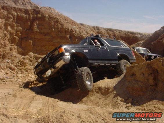 Black Ford Bronco off-roading on a dirt hill, front-left tire lifted