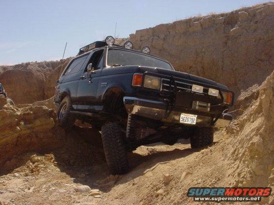 Black Ford Bronco climbing a dirt hill, aftermarket bumper and lights visible
