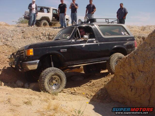 Black 1988 Ford Bronco navigating a rocky off-road trail with a white Bronco in the background