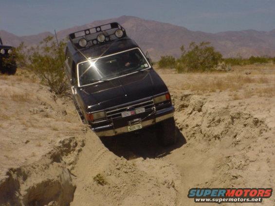 Black Ford Bronco with roof lights driving off-road, tilted in a dirt ditch