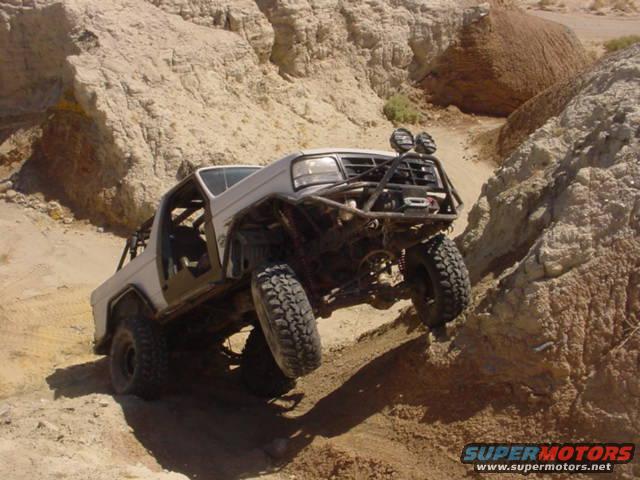Modified 1988 Ford Bronco climbing a steep dirt embankment, front grille guard and roll cage visible