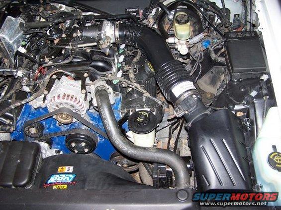 Engine bay with air intake tube, alternator, and hoses visible. Some text on hoses and a sticker on the fan shroud