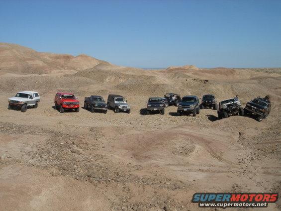 group of SUVs and trucks parked in a desert with hills in background