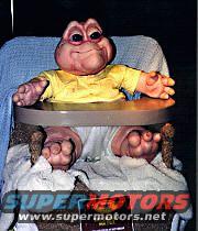 Baby Sinclair in a high chair, with 'SUPERMOTORS www.supermotors.net' text at the bottom