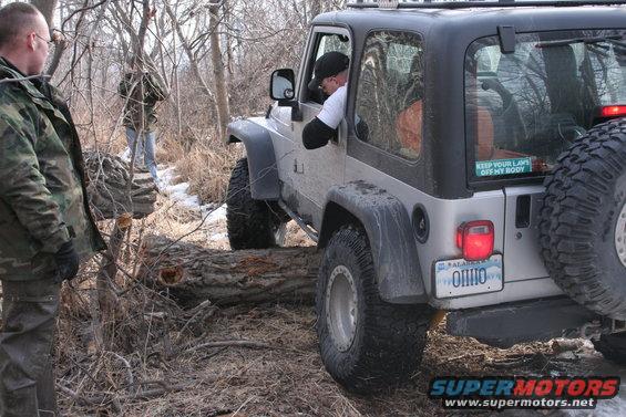 Silver Jeep Wrangler with a spare tire on the back, driving over a fallen tree. Ohio license plate visible