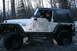 1995 Jeep Cherokee - A driver steers a muddy Jeep Rubicon through a challenging off-road course in a wooded area.