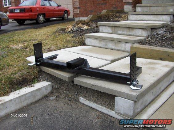 Black metal tow hitch receiver and parts on concrete steps. Red sedan in background