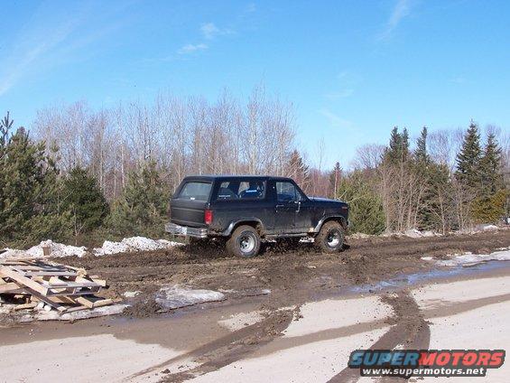 Black SUV with lifted suspension driving through mud and trees in background