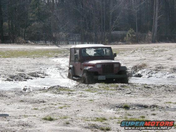 Red Jeep Wrangler driving through mud puddle