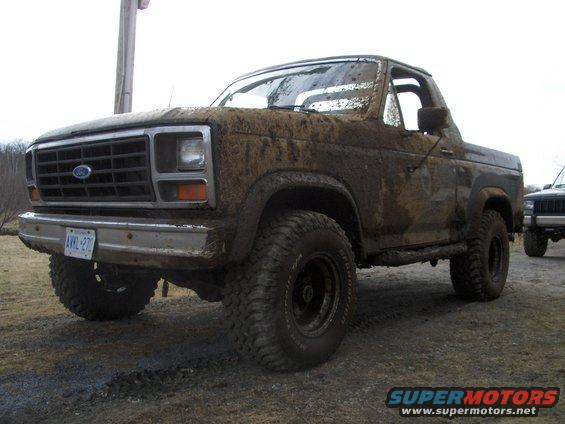1986 Ford Bronco covered in mud, front 3/4 view. License plate visible