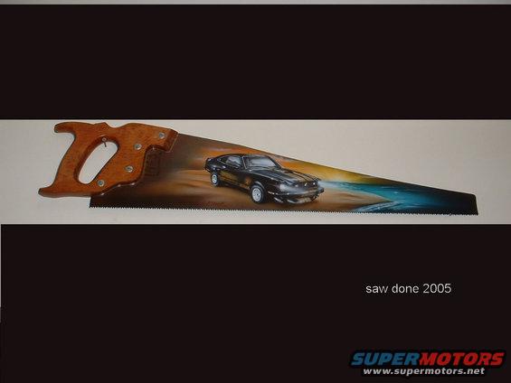 Hand saw with a painted scene of a black car on a beach, text 'saw done 2005' and 'SUPERMOTORS' logo