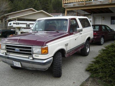 Two-tone maroon and white Ford Bronco parked in driveway, front-left view